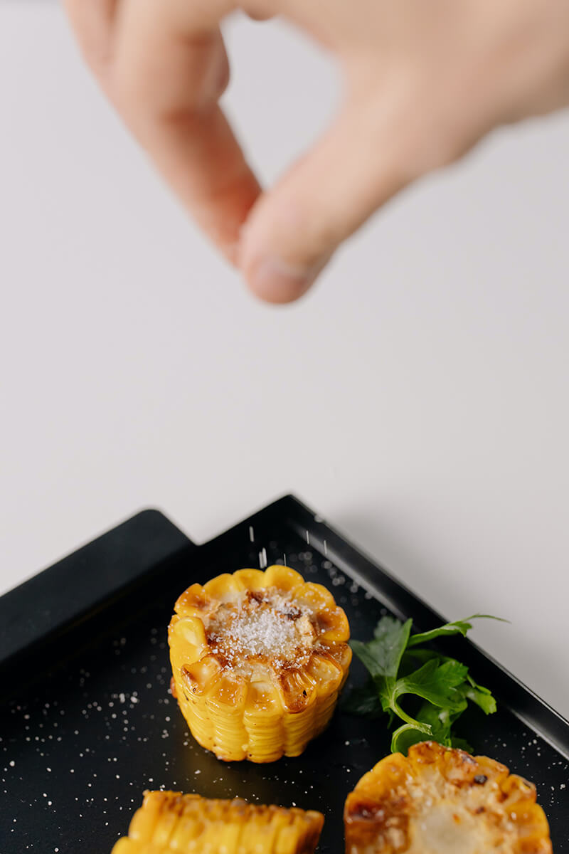 Colores y propiedades de las frutas y verduras. Maíz a la plancha con mano que le echa sal