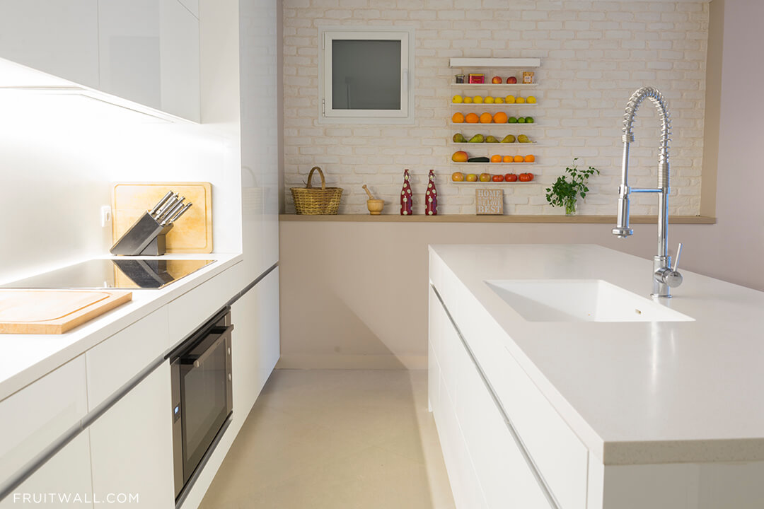 Fruitwall, los mejores fruteros modernos y de diseño para la cocina, colocado en una cocina sobre pared de ladrillo blanca. esta lleno de muchas frutas y verduras.